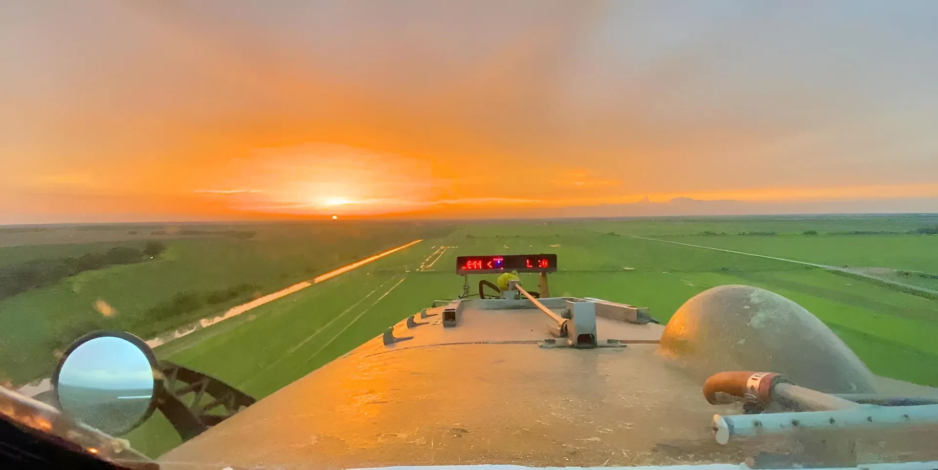 View from the cockpit of an agricultural aircraft at sunset over green fields