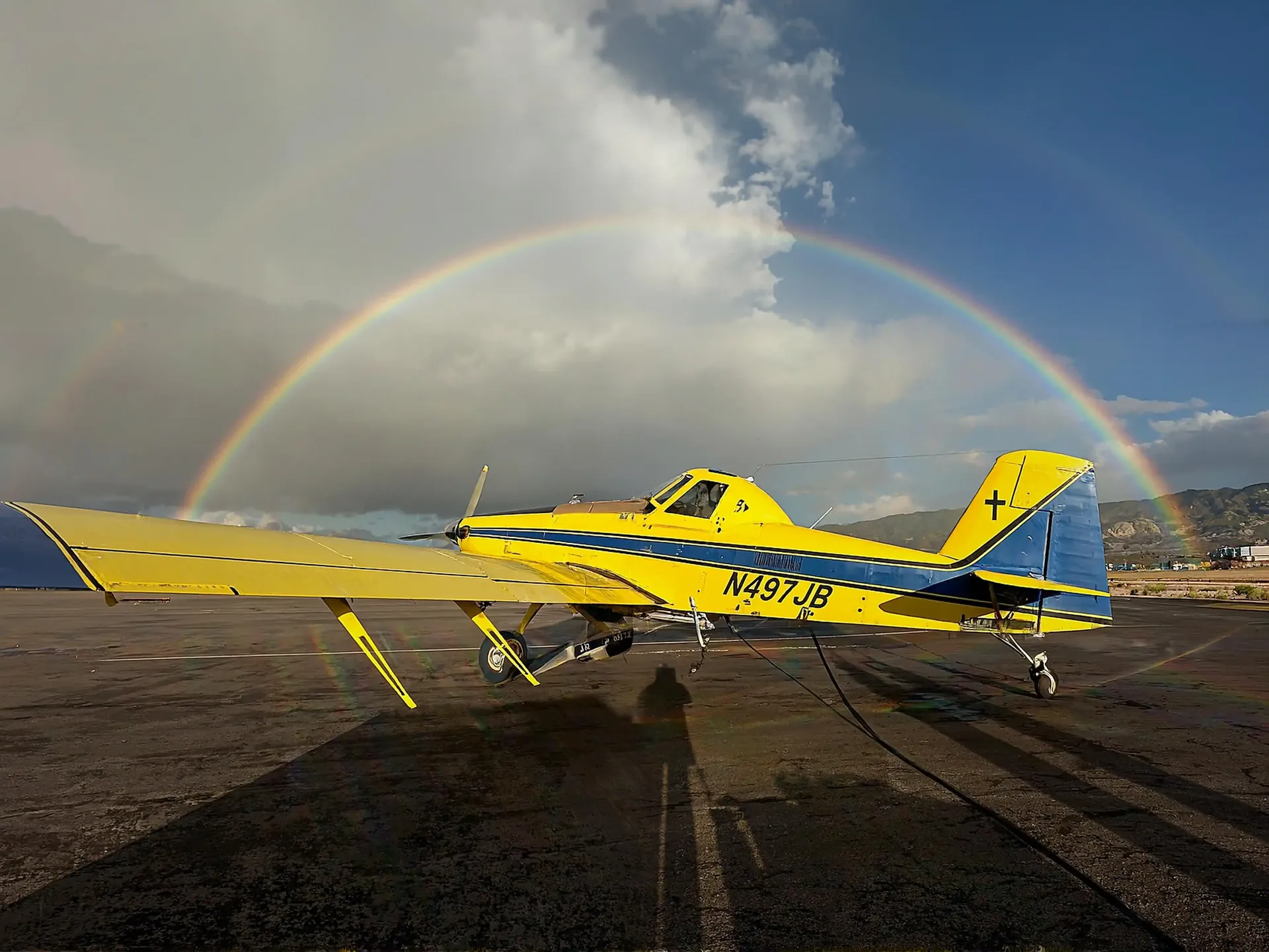 The yellow and blue Agri-Land Aviation aircraft on the ramp under a rainbow
